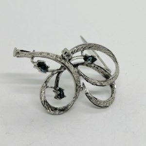 Broche argent façon ruban, ouvragée et sertie de saphirs navettes.